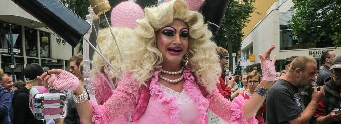 A drag queen dressed in pink, walking through a crowd.